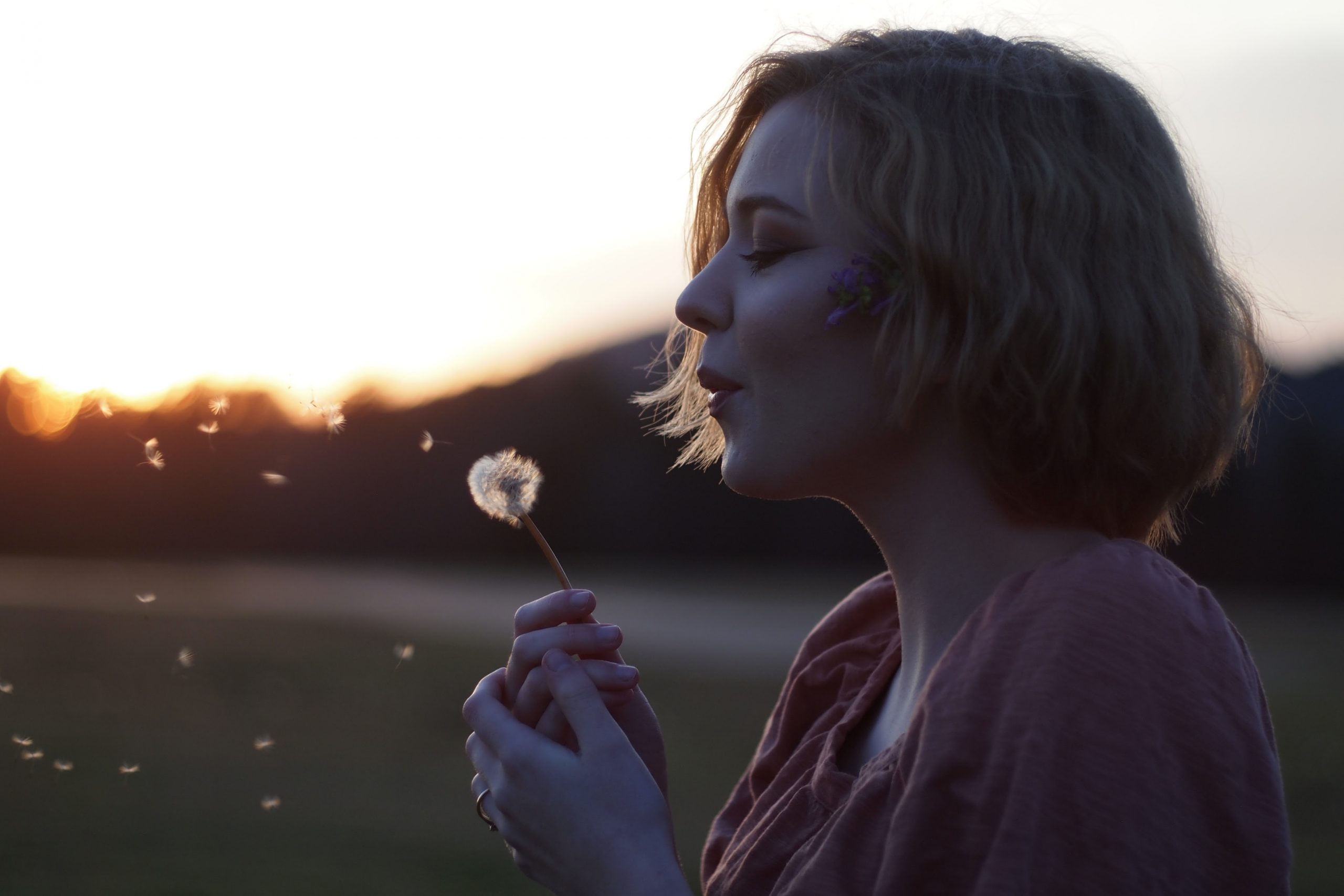 woman blowing dandelion seeds